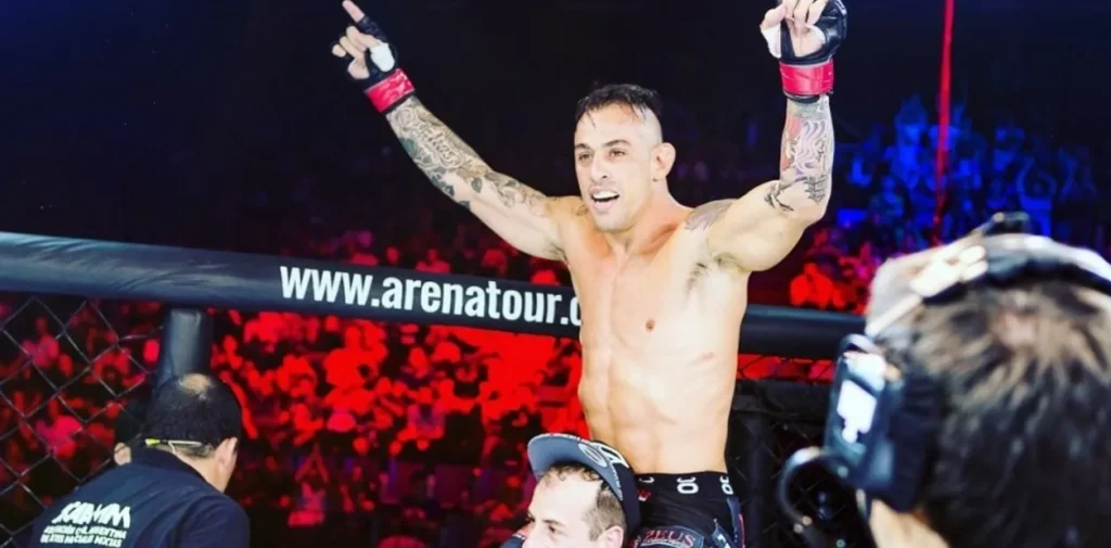 title="Coach Javier Oyarzabal wins MMA fight – Brazilian Jiu-Jitsu black belt in Miami" alt="Coach Javier Oyarzabal, Brazilian Jiu-Jitsu black belt in Miami, celebrates MMA victory inside the cage at Mario Sperry Academy"
